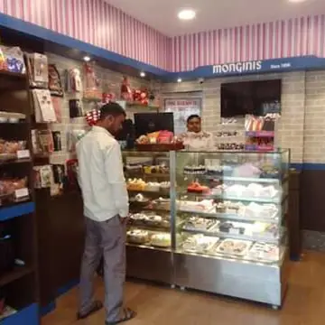 Customer at a glass cake display counter inside a Monginis shop